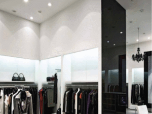 A modern clothing store interior features racks of clothes, shelves with bags, white walls, and a black accent wall illuminated by energy-efficient Range LED Bulb 18W spotlights.